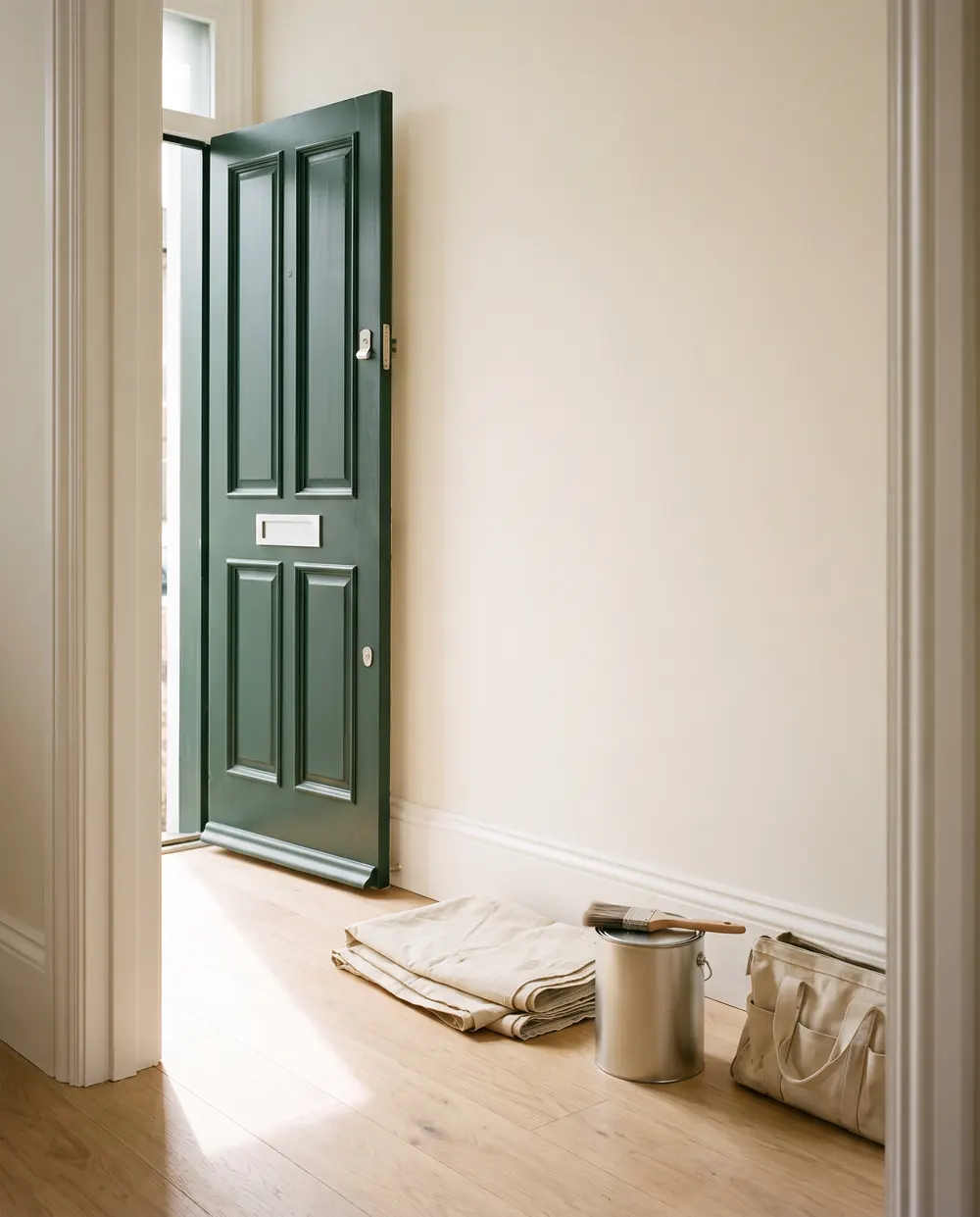 Freshly finished hallway with a green front door, new skirting and a folded dust sheet