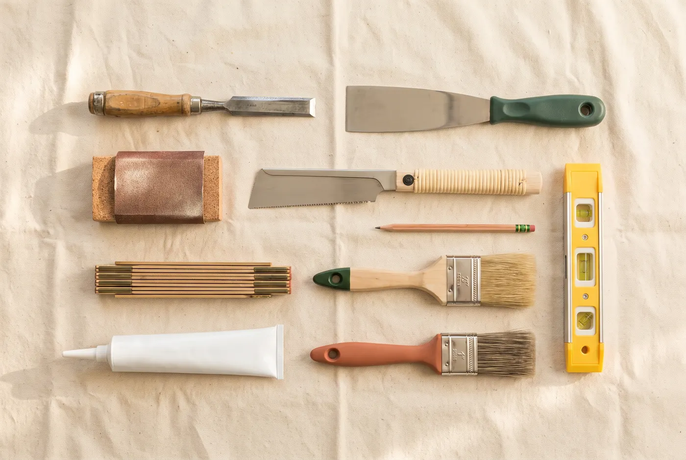 Finishing tools laid out on a dust sheet: chisel, filling knife, pull saw, brushes, caulk and a spirit level